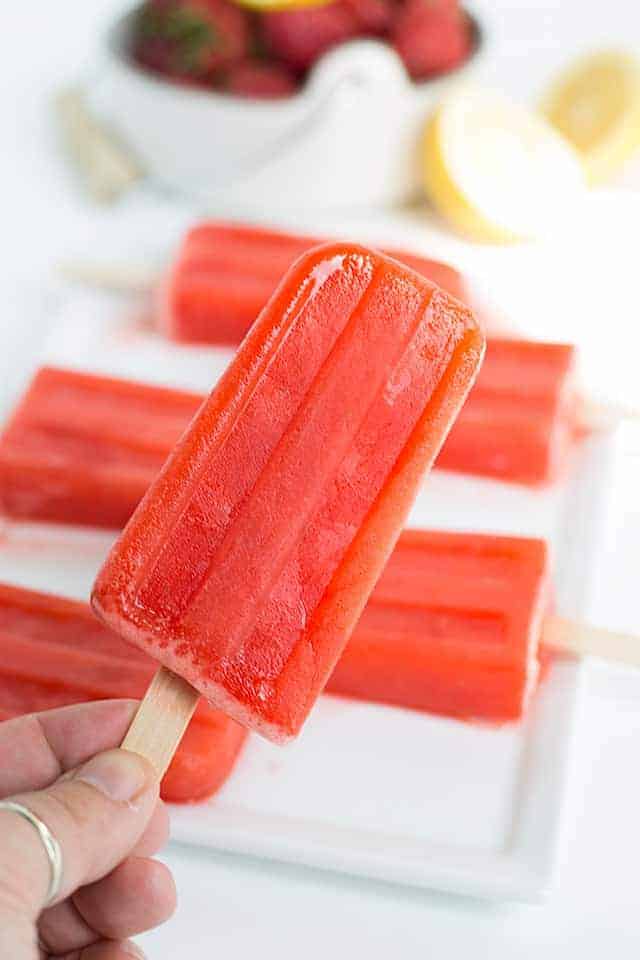 holding a strawberry lemonade popsicle with popsicles on a plate in the background