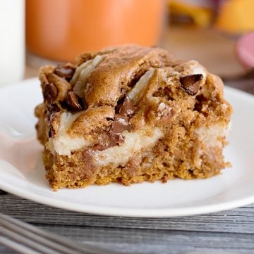 Pumpkin cheesecake bars on a white plate with a hint of the Pumpkin Earthquake Cake.