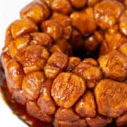 A delightful monkey bread made with frozen bread dough, showcasing caramelized pieces arranged in a ring on a white plate, complemented by an orange napkin underneath. The perfect Monkey Bread Recipe for an easy and delicious treat!.
