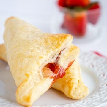 turnovers on a white plate with strawberries behind it