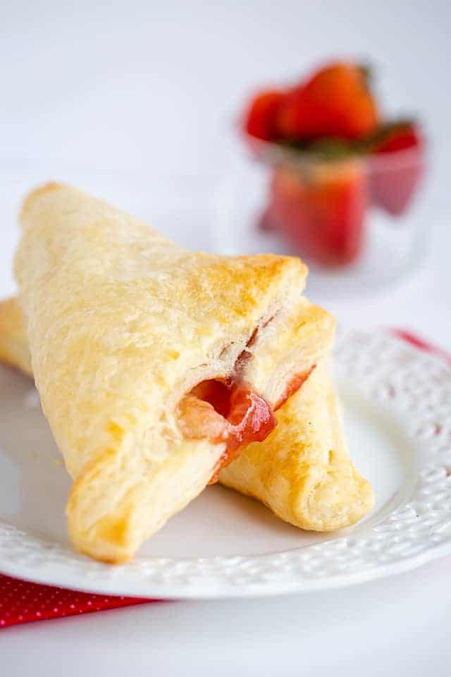 turnovers on a white plate with strawberries behind it
