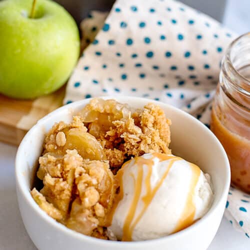 white bowl of caramel apple crisp with vanilla ice cream