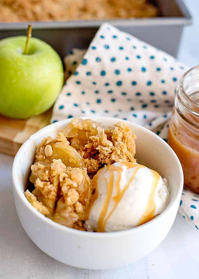 white bowl of caramel apple crisp with vanilla ice cream