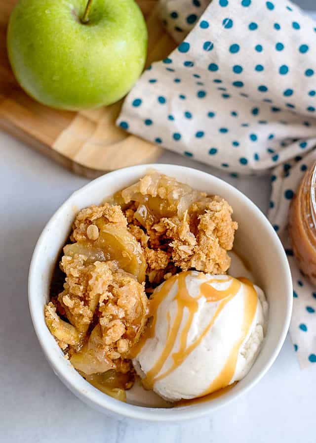 overhead shot of caramel apple crisp in white bowl with ice cream and caramel sauce