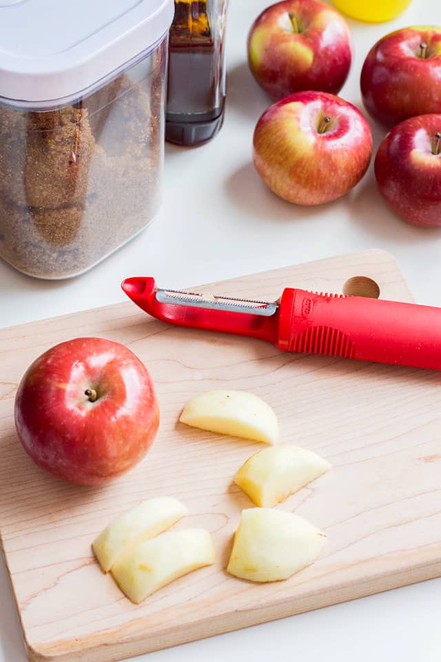 apple peeler, apples, and apple slices on a cutting board.