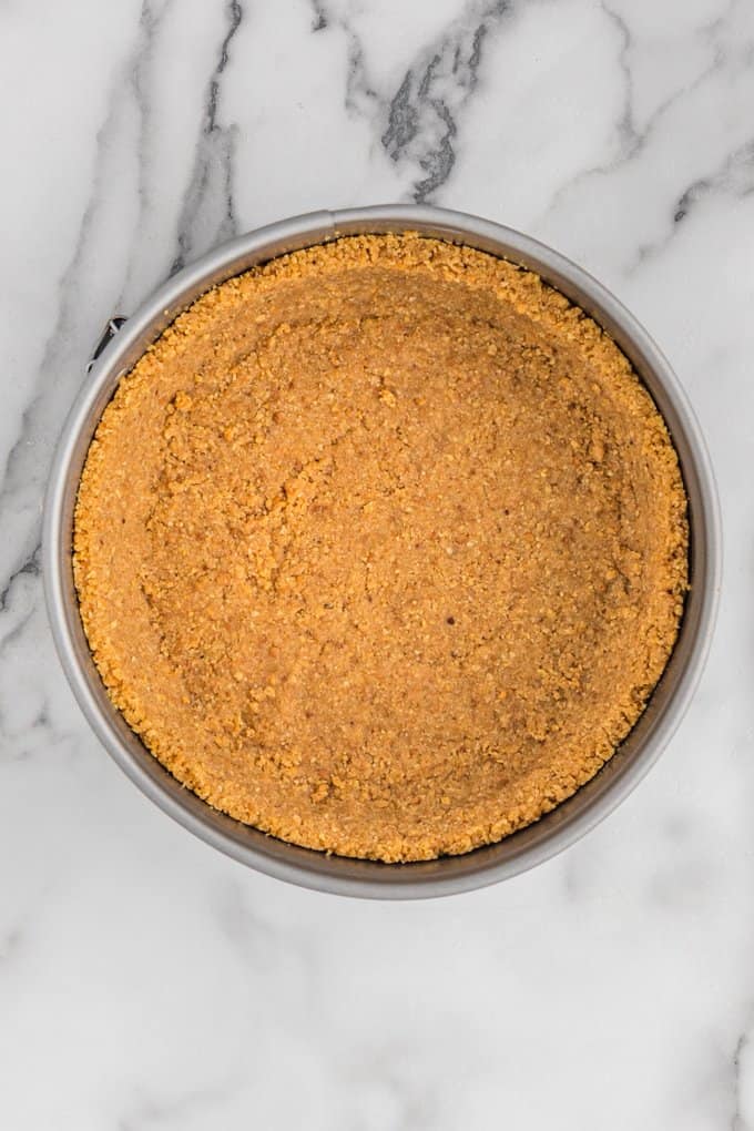 baking pan with a graham cracker crust in it on a marble surface