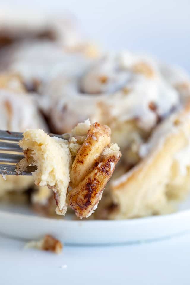 Fork full of bananas foster cinnamon roll with cinnamon roll behind it