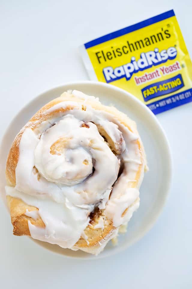 Bananas Foster Cinnamon Roll on a small white dessert plate with a packet of yeast next to it