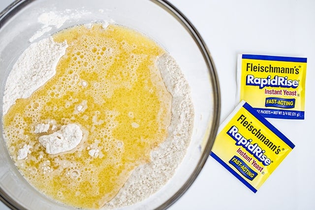 glass bowl with flour, yeast, and butter with packets of yeast beside it