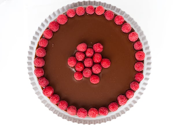 horizontal shot of chocolate raspberry cheesecake on a white cake plate with a white background