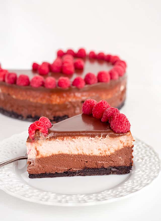 slice of chocolate raspberry cheesecake on white plate with whole cheesecake behind it