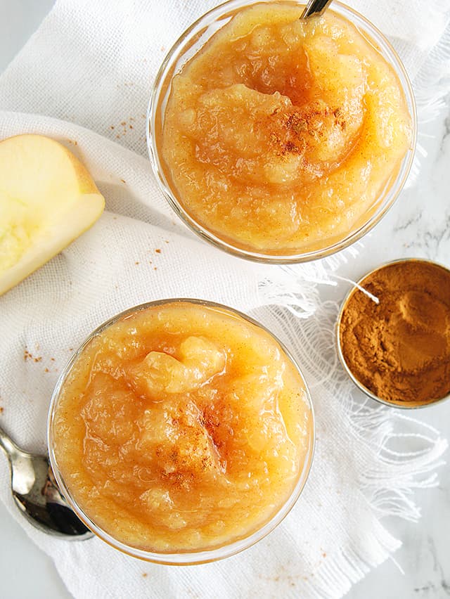 two small bowls of instant pot applesauce with ground cinnamon, apple slice, and white linen