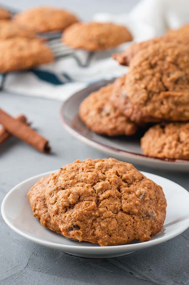 two pumpkin oatmeal chocolate chip cookies on white plate with a stack of cookies behind it