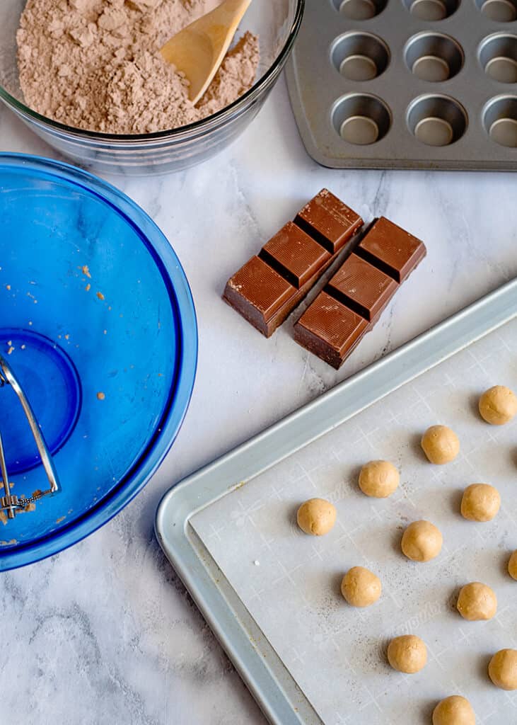 peanut butter balls on a baking sheet in a blue mixing bowl and almond bar next to the sheet