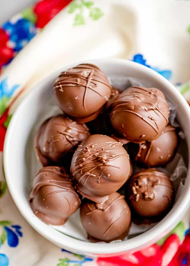 peanut butter balls stacked in a white bowl with a floral linen underneath