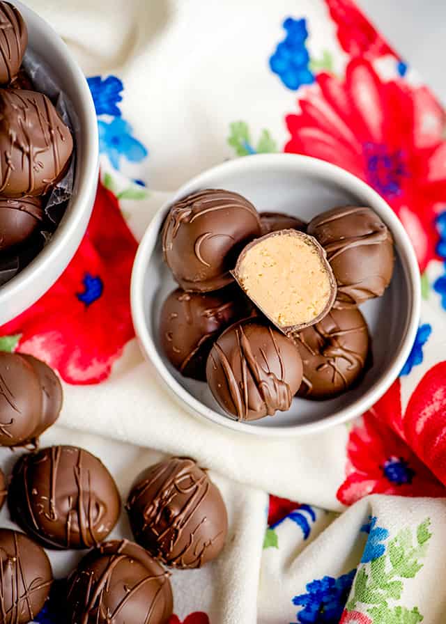 small bowl of peanut butter balls with other peanut butter balls scattered around it on a floral linen