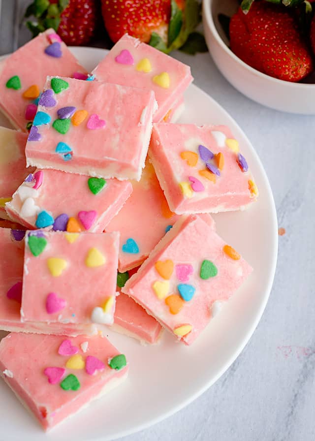 stack of strawberries and cream fudge on a white plate with a bowl of strawberries