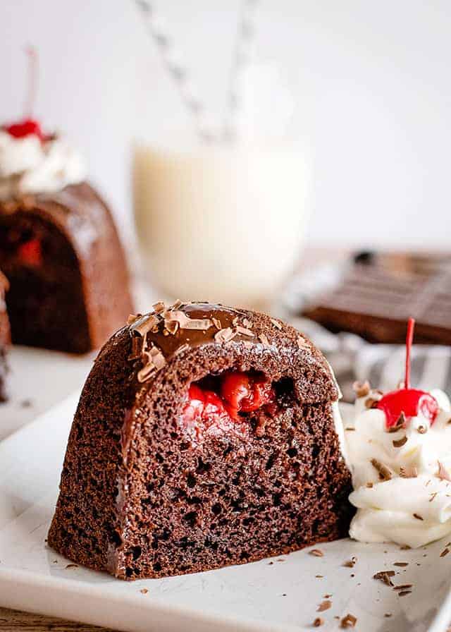 slice of chocolate cherry bundt cake with whipped cream and cherry on white plate