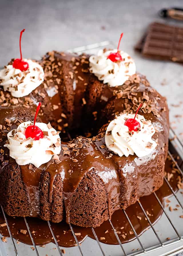 chocolate cherry bundt cake with whipped cream and cherries on a wire rack