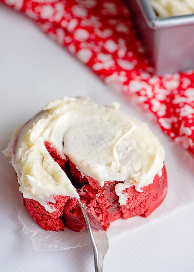 fork cutting a red velvet cinnamon roll in half on white background