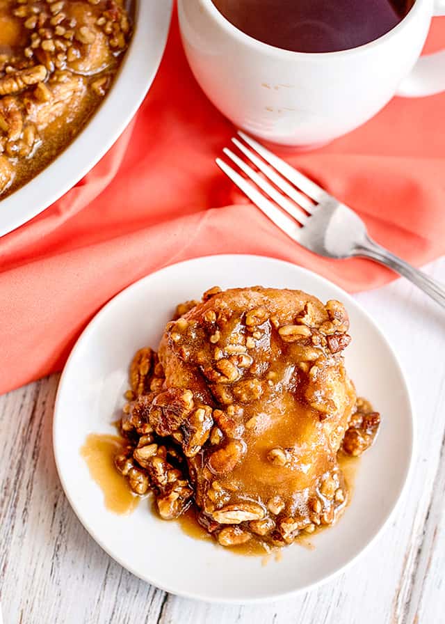 overhead view of sticky bun on a small white plate with a fork and pink fabric