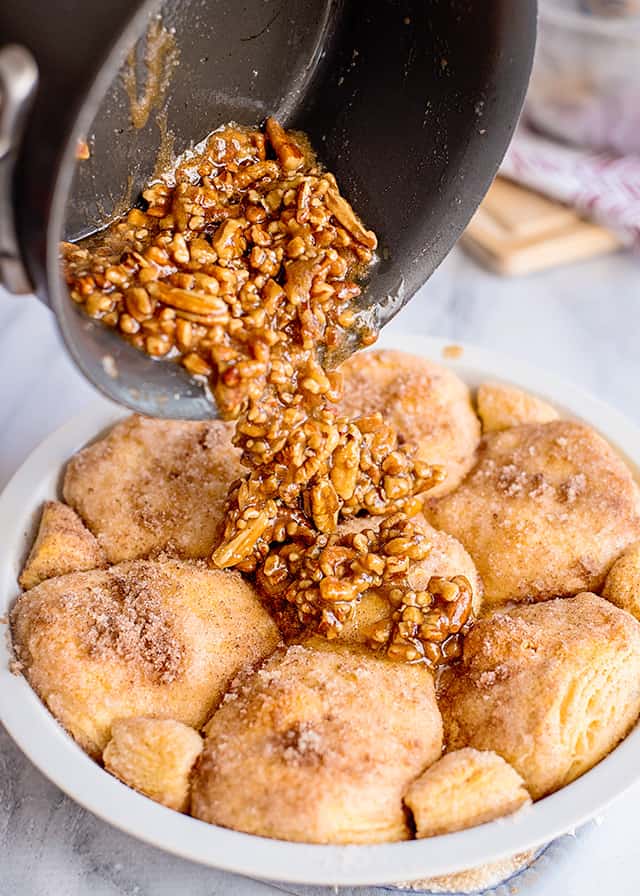 pan of maple brown sugar sauce with pecans being pourced onto the baked sticky buns