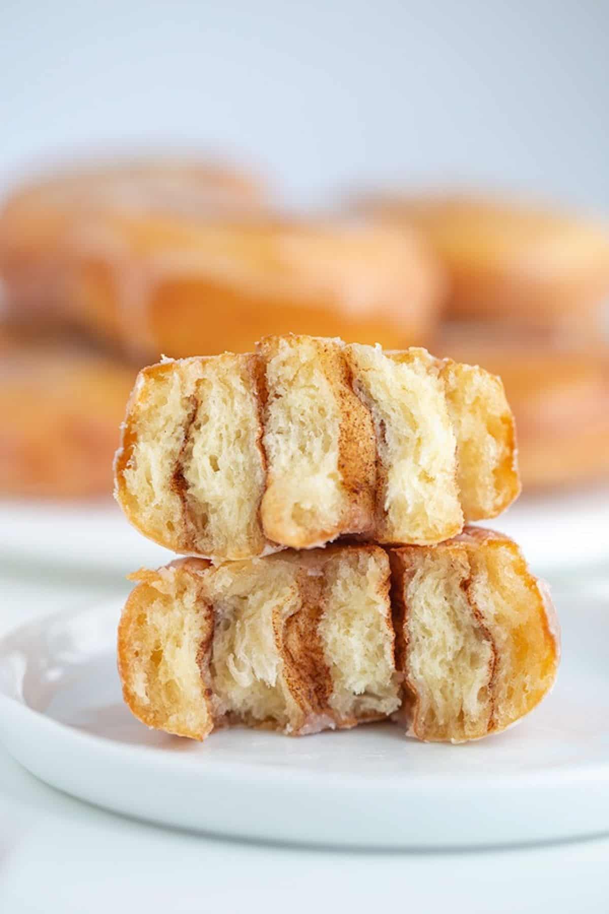 Two halves of a glazed honey bun cinnamon roll stacked on a white plate.