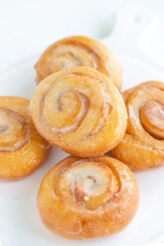A stack of five glazed honey bun cinnamon rolls on a white plate.