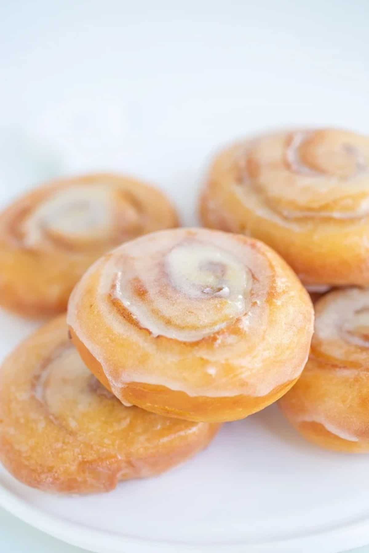 A pile of glazed honey buns on a white plate.
