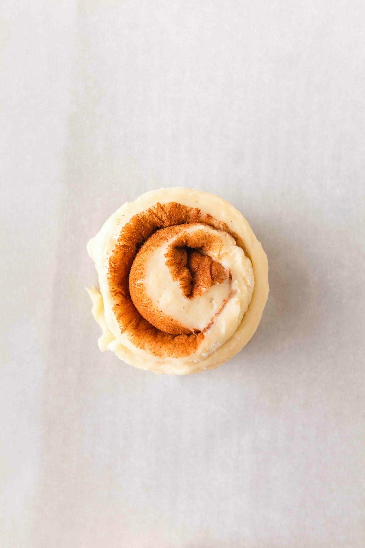 A single honey bun cinnamon roll with white icing on parchment paper.