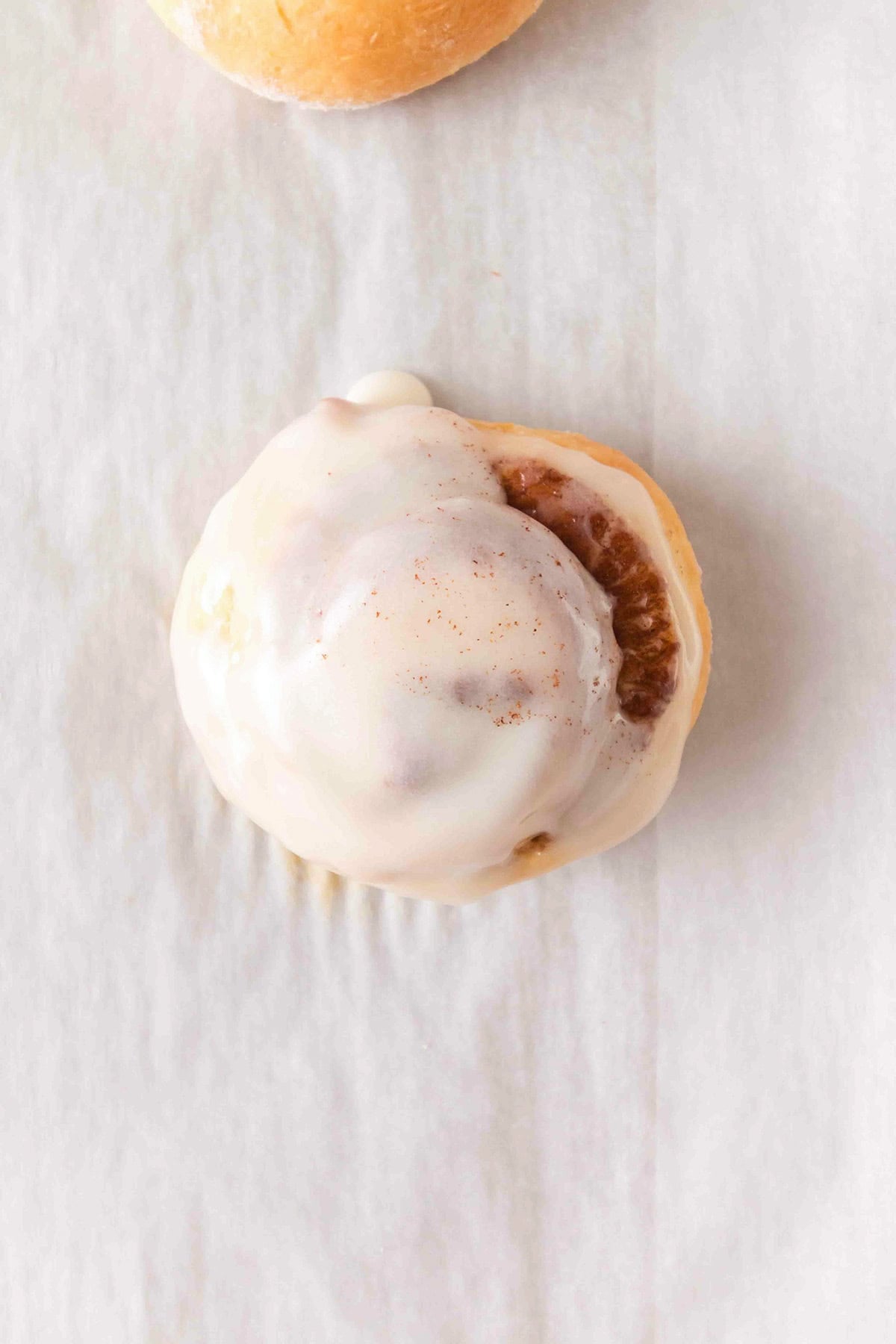 A single honey bun topped with white icing on parchment paper.