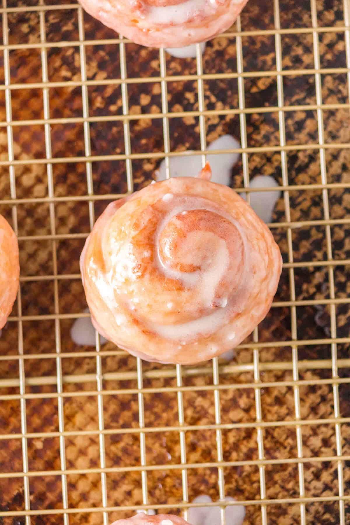 Glazed honey bun cinnamon roll on a wire cooling rack.