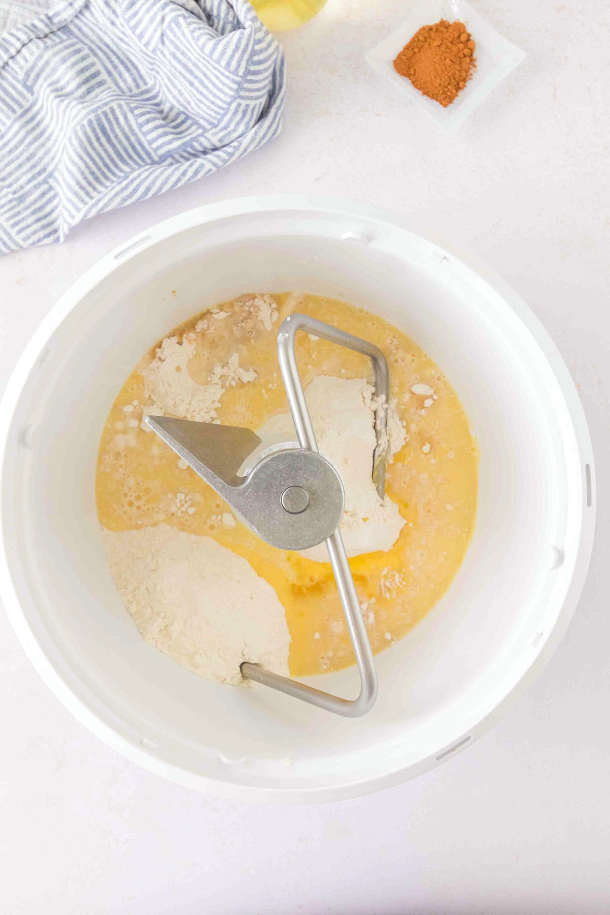 A stand mixer bowl containing flour and a yellow liquid for honey buns, with a dough hook attachment.