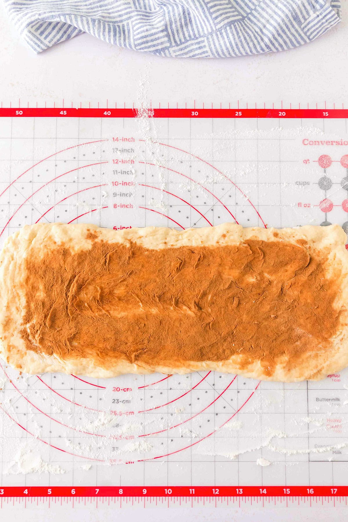 A rectangular sheet of honey bun dough coated in cinnamon on a silicone baking mat.