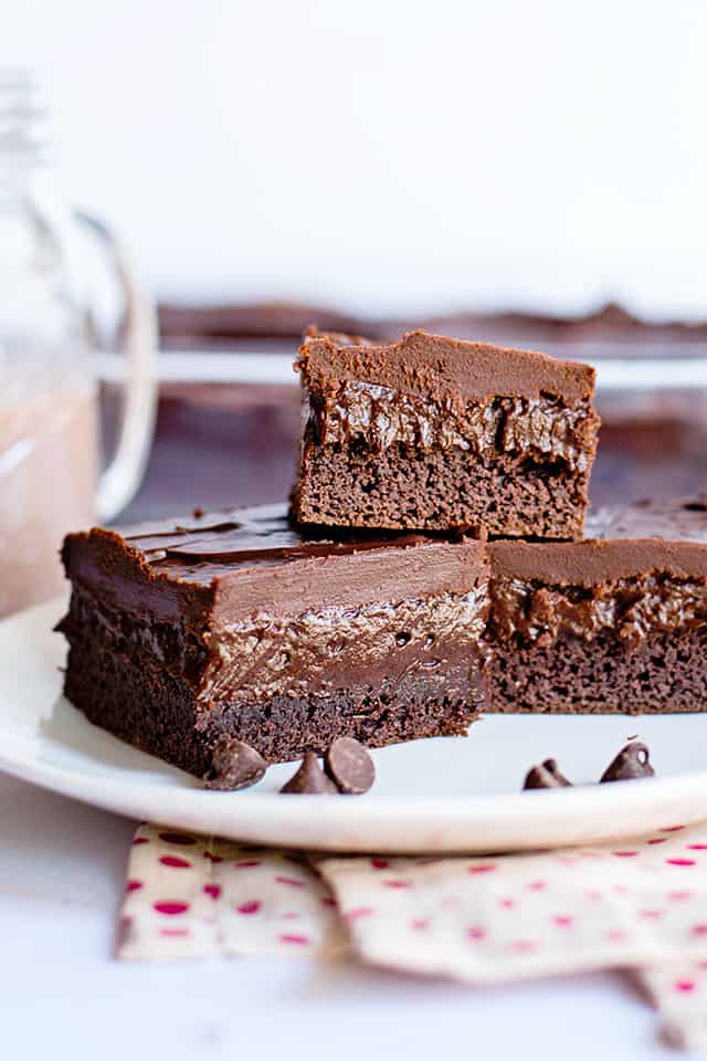 chocolate pudding bars stacked on a white dessert plate with chocolate chips and polkadot fabric under the plate