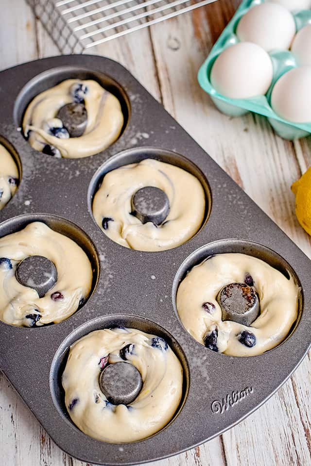 donut pan with donut batter piped in each cavity and eggs beside pan