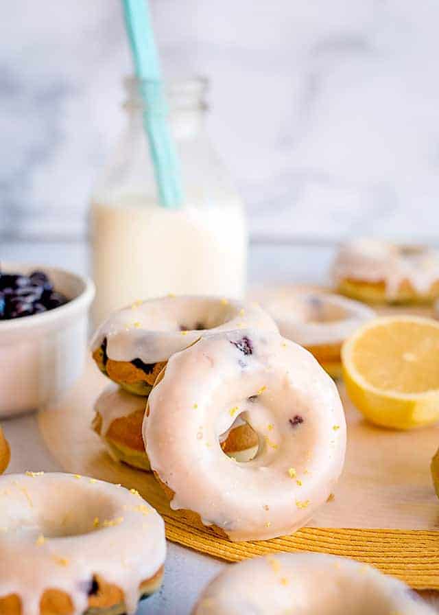a lemon blueberry donut propped up against a stack of donuts with milk behind it