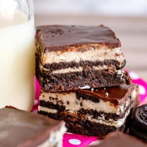 cookies and cream oreo brownies stacked on top of eachother next to a glass of milk with a pink fabric under them