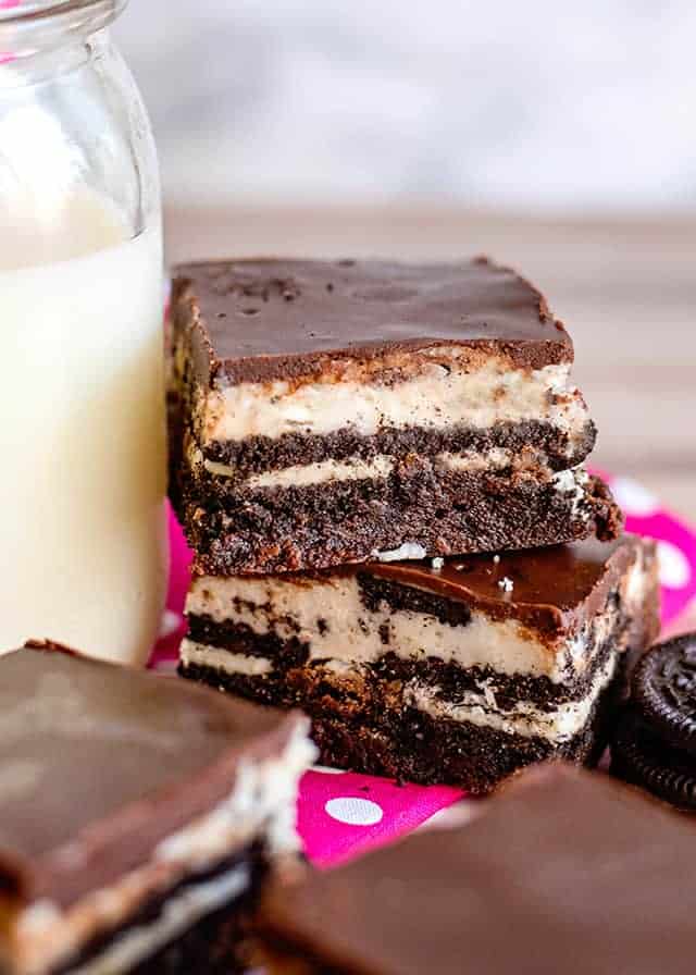 cookies and cream oreo brownies stacked on top of eachother next to a glass of milk with a pink fabric under them