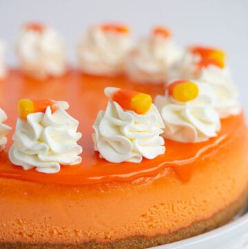 whole candy corn cheesecake on a white plate with whipped cream and candy on top