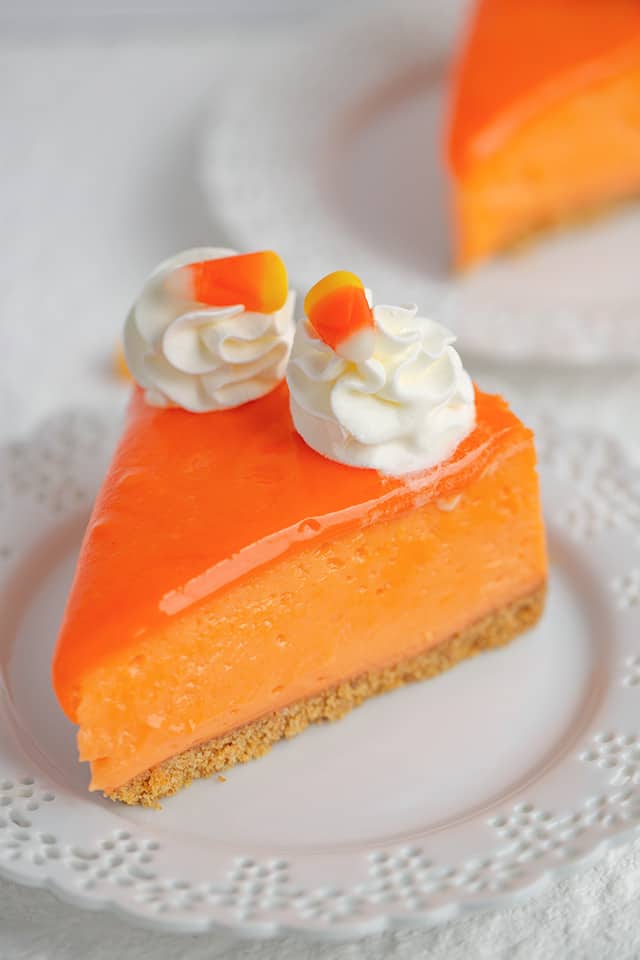 slice of candy corn cheesecake on a white plate with a second slice behind it