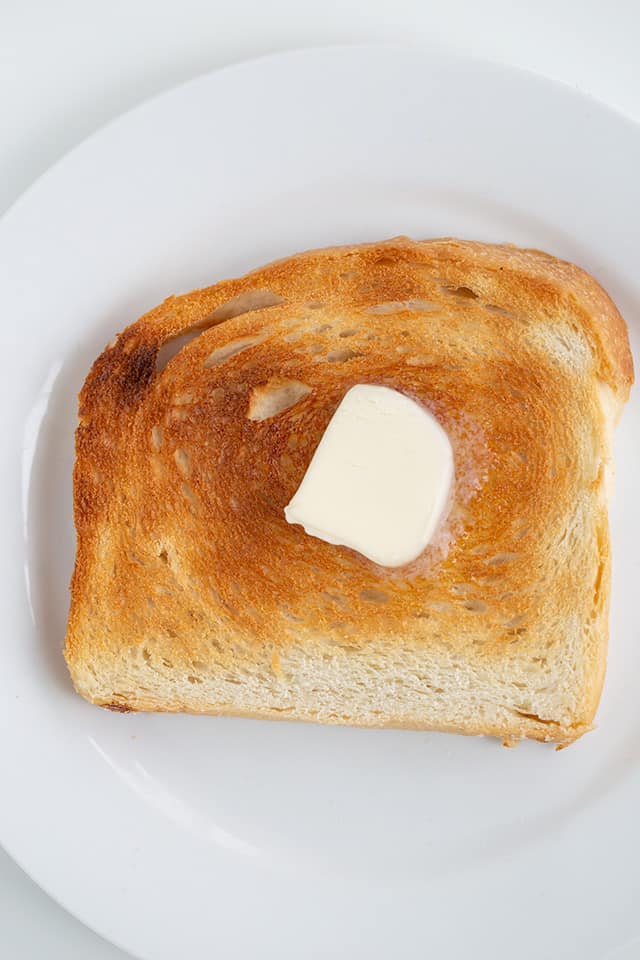 slice of toasted bread on a white plate with a dab of butter in the center