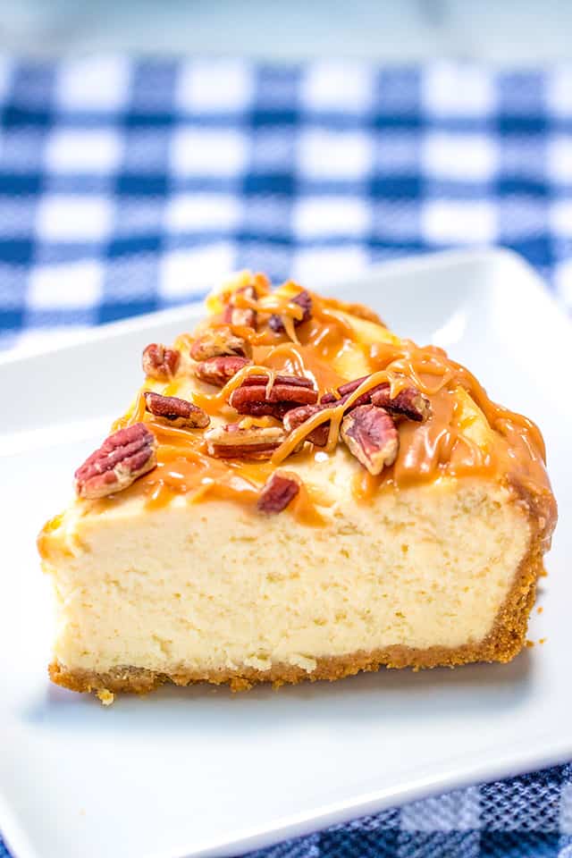 slice of salted caramel cheesecake on a white square plate with a blue plaid fabric