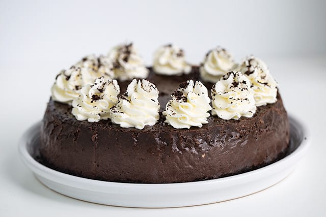 horizontal image of full cheesecake on a white serving plate with swirls of whipped cream