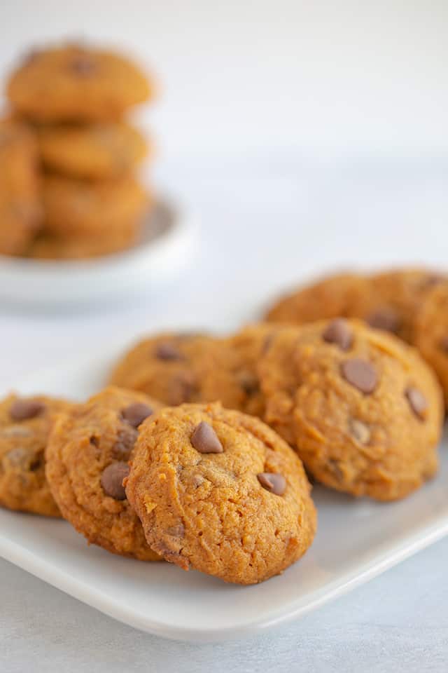 plate of pumpkin cookies with a stack of cookies on a white plate in the background