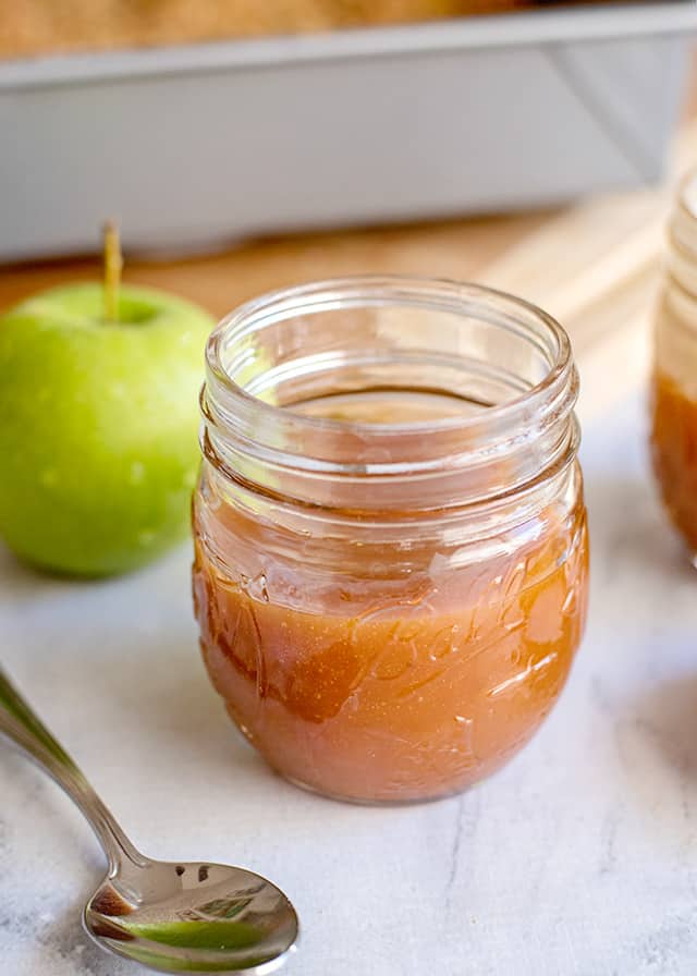 jar of caramel sauce with a spoon and apple