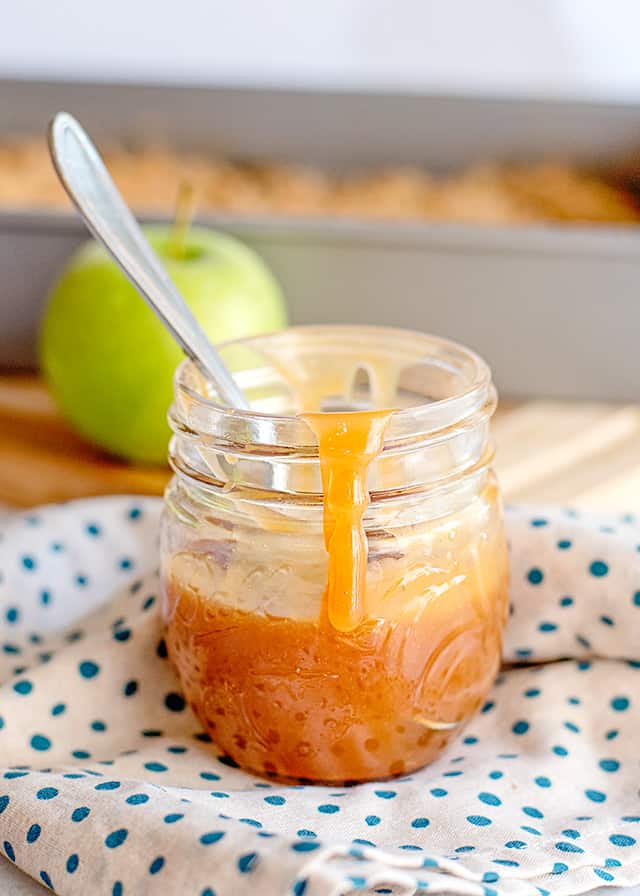 jar of caramel sauce with caramel dripping down it on a white and blue polkadotted linen