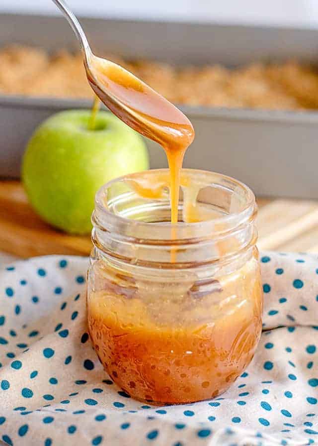 spoon full of caramel sauce dripping into a jar