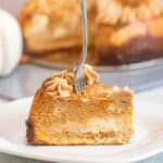 slice of pumpkin cheesecake on a white plate with the rest of the cheesecake behind it