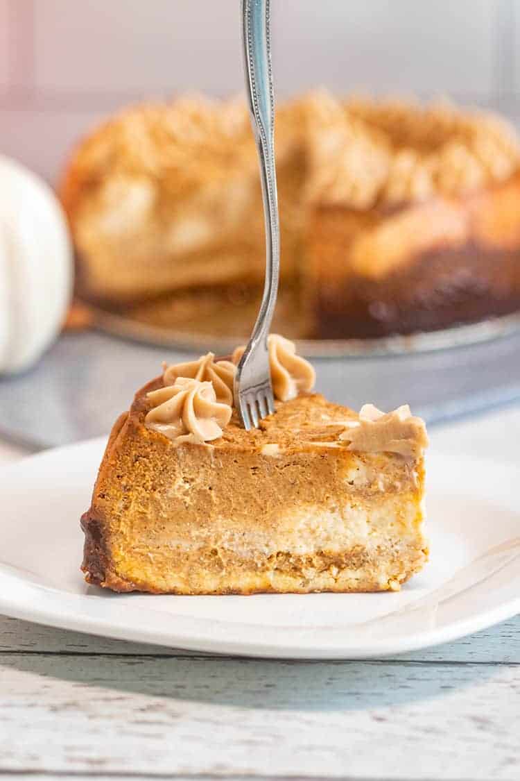 slice of pumpkin cheesecake on a white plate with the rest of the cheesecake behind it